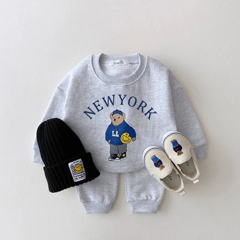 Kids gray New York sweatshirt and pants set with bear graphic, black beanie, and white slip-on shoes