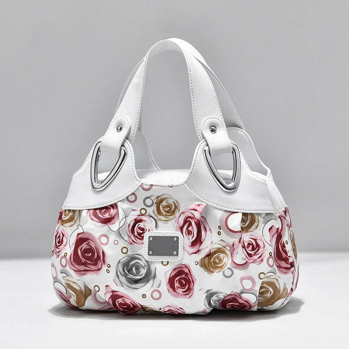 White floral handbag with pink, gold, and gray rose patterns and silver buckle accents