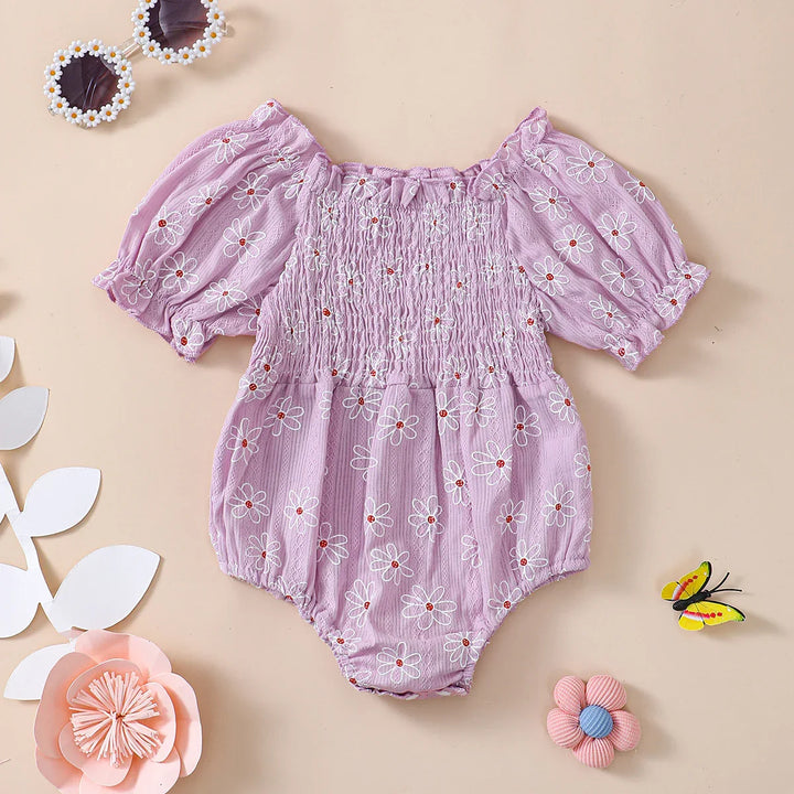 Lilac baby romper with white daisy embroidery and puff sleeves, styled with flower and butterfly props