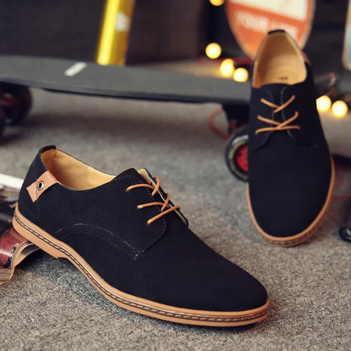 Black casual men's shoes with brown laces and sole on carpeted floor, skateboard in background