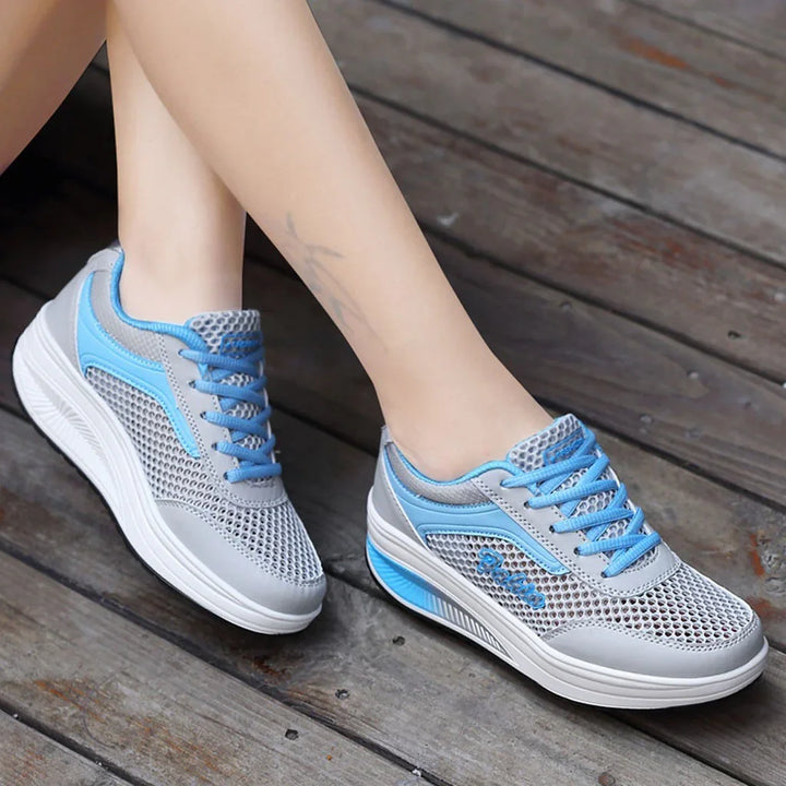 Light gray and blue mesh sneakers with thick white soles worn on wooden floor