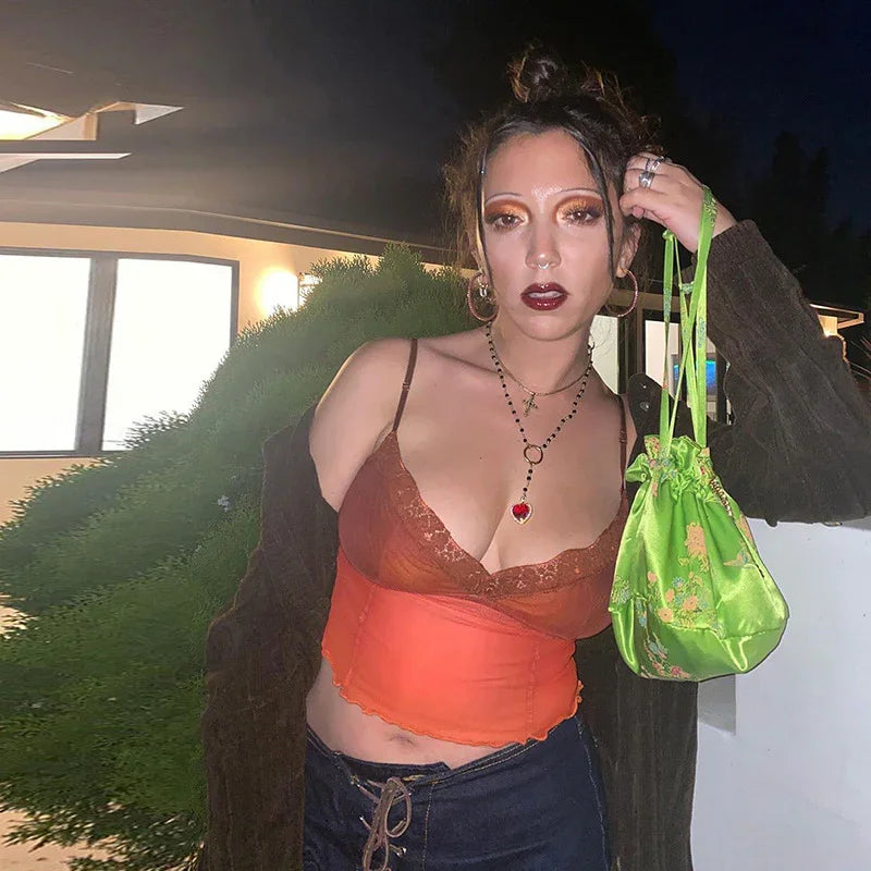 Young woman in orange lace top and dark cardigan holding green floral purse outdoors at night