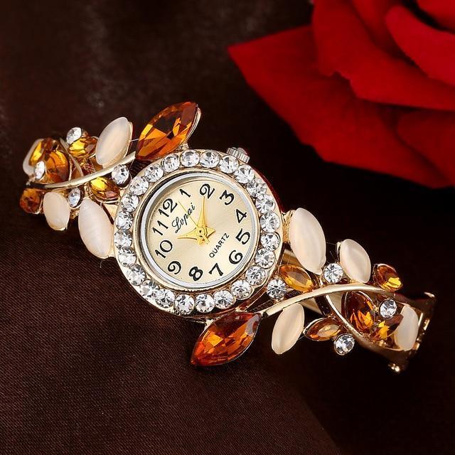 Elegant gold-tone quartz wristwatch with crystal bezel and amber leaf accents on dark background