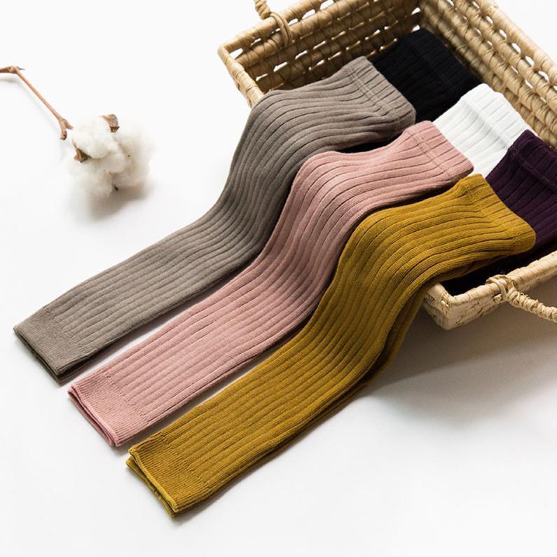 Ribbed knit leggings in brown, pink, mustard, black, white, and purple colors displayed in a woven basket with cotton branch