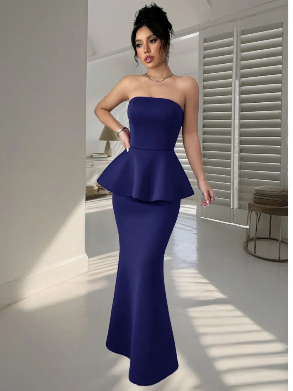 Woman in elegant strapless navy blue peplum evening gown in modern minimalist room