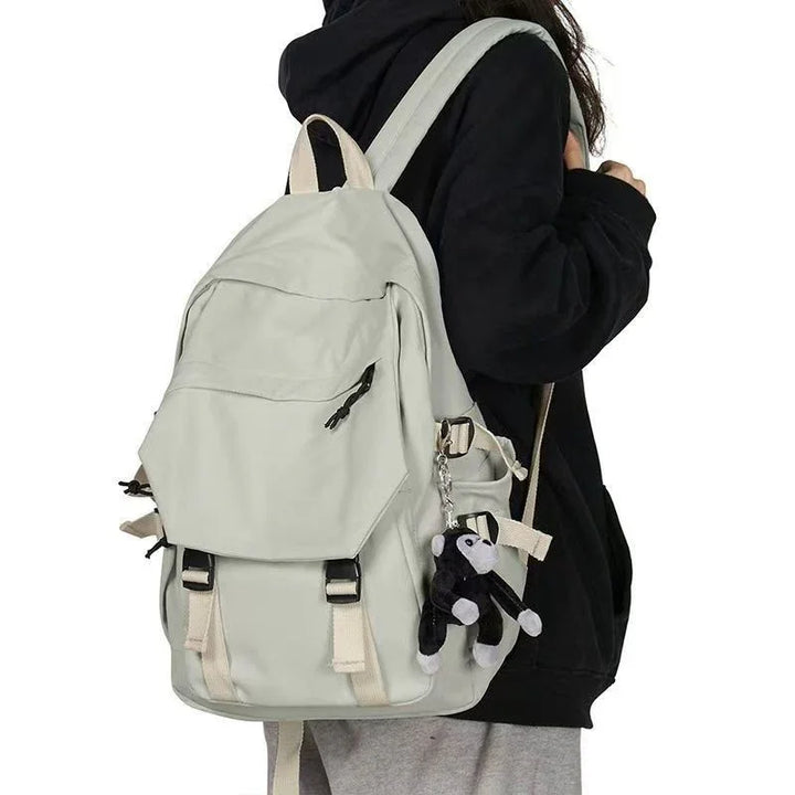 Person wearing light gray backpack with front zipper pocket and a black monkey keychain attached