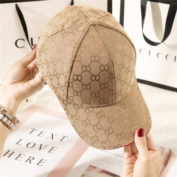 Beige Gucci designer baseball cap with interlocking GG pattern held by person with red nail polish and luxury shopping bags