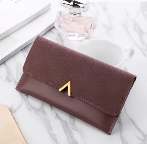 Elegant brown leather wallet with gold triangular clasp on marble surface with perfume bottle and white cup