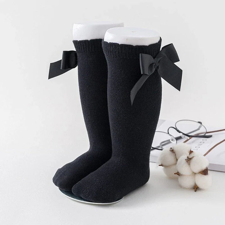 Black knee-high socks with decorative black bows displayed on white mannequin legs