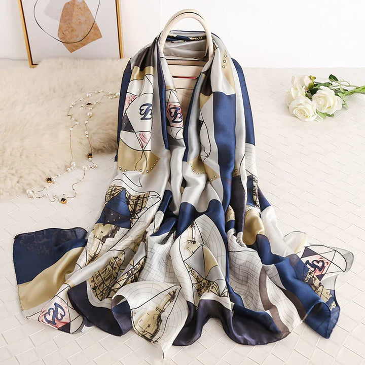 Silky patterned scarf in blue, beige, and white draped over handbag on white textured surface with white roses