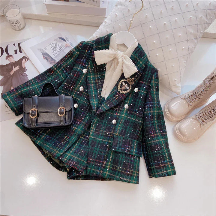 Child's green plaid double-breasted blazer with white pearl buttons, cream bow blouse, black buckle bag, and beige lace-up boots