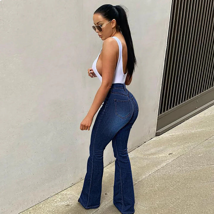 Woman wearing white tank top and high-waisted blue flare jeans walking outdoors near wall