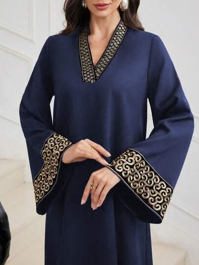 Woman wearing navy blue long sleeve dress with ornate gold embroidery on cuffs and neckline