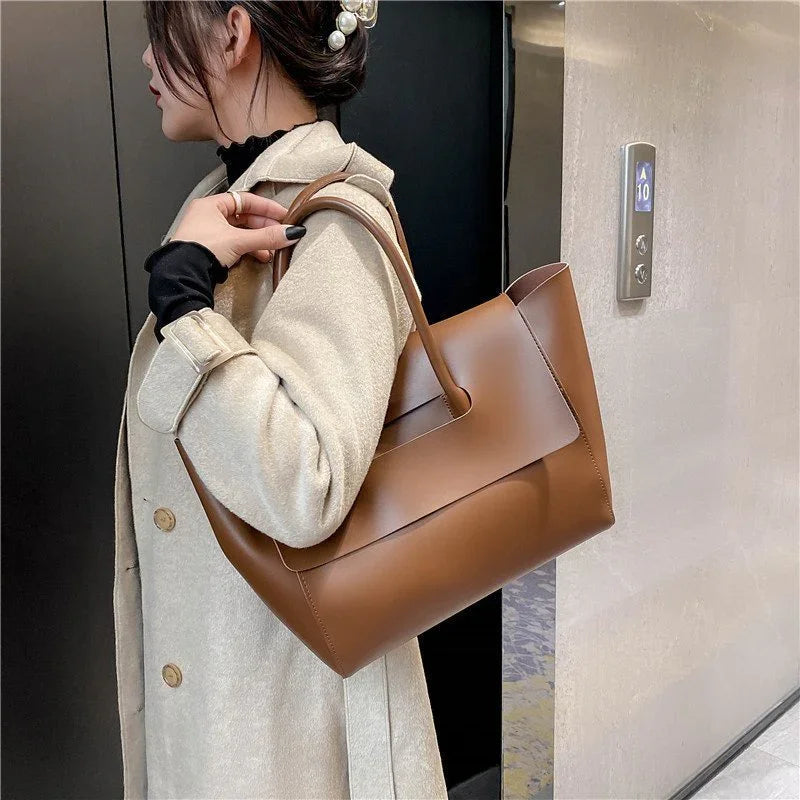 Woman in beige coat carrying a large brown leather tote bag with pearl hair accessory