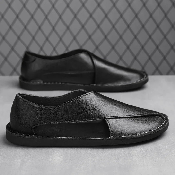 Black leather slip-on casual shoes with cutout design and visible stitching on gray surface