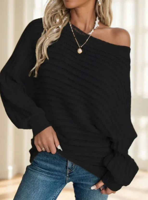 Woman wearing off-shoulder black knit sweater paired with blue jeans and gold pendant necklace