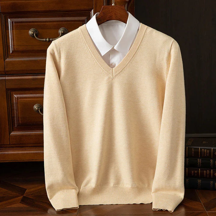 Beige V-neck sweater layered over white collared shirt, displayed on wooden hanger against wooden drawers