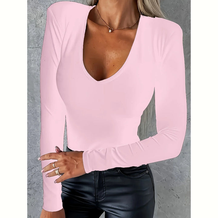 Woman wearing fitted light pink v-neck long sleeve top and black leather pants, textured gray background