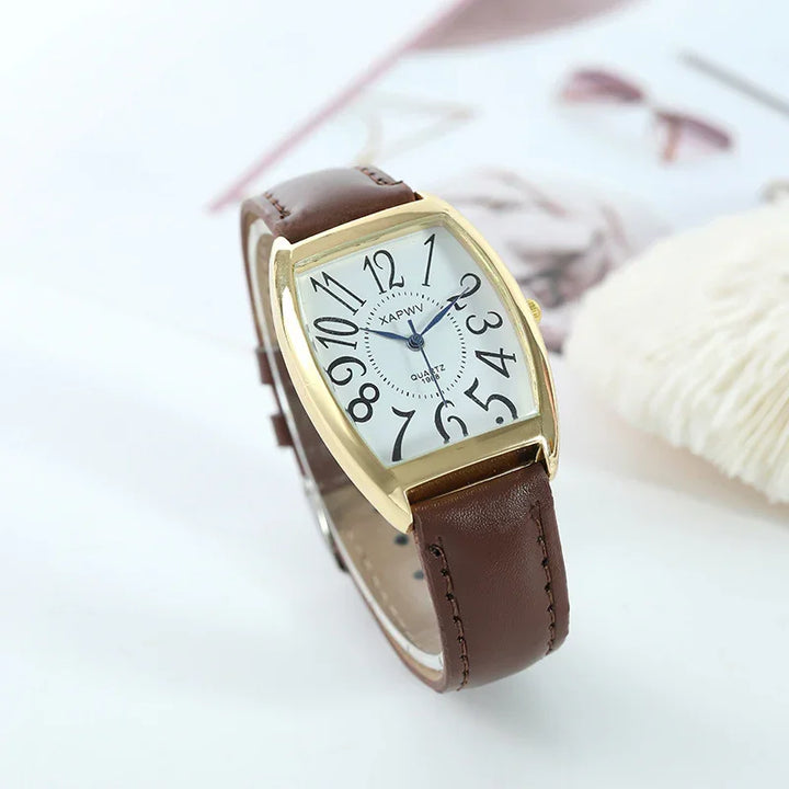 Gold case wristwatch with large black numbers and brown leather strap on white surface