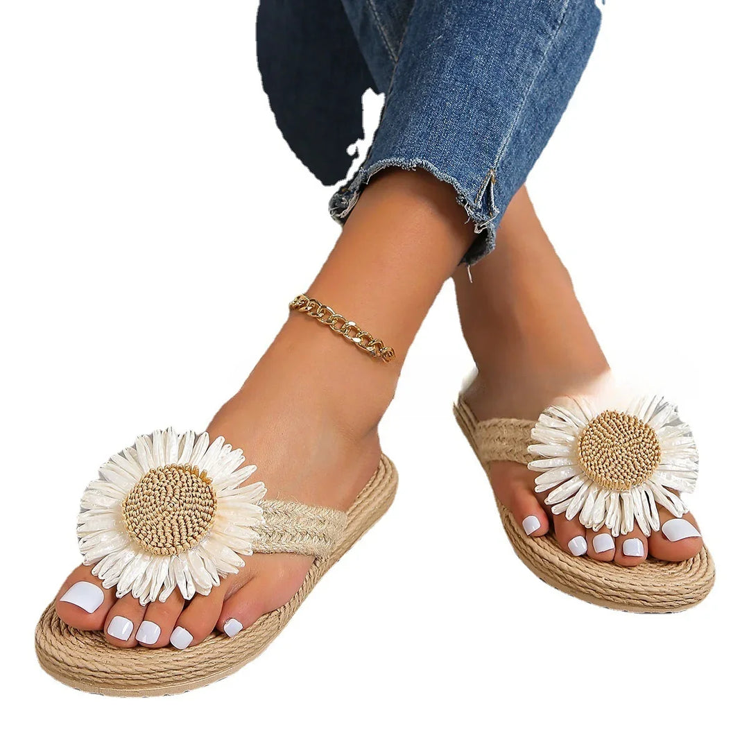 Feet wearing beige woven sandals with large white daisy flowers and gold ankle bracelet