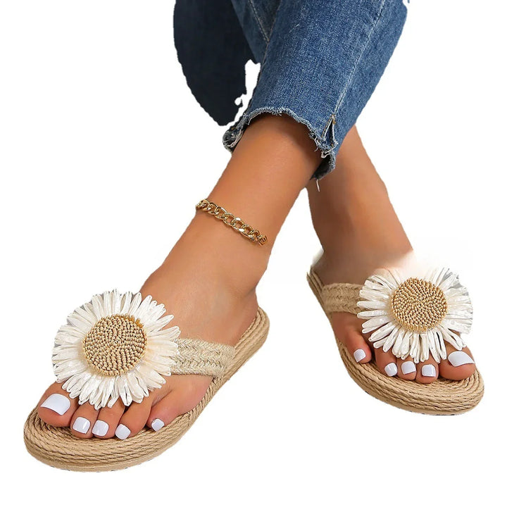 Feet wearing beige woven sandals with large white daisy flowers and gold ankle bracelet