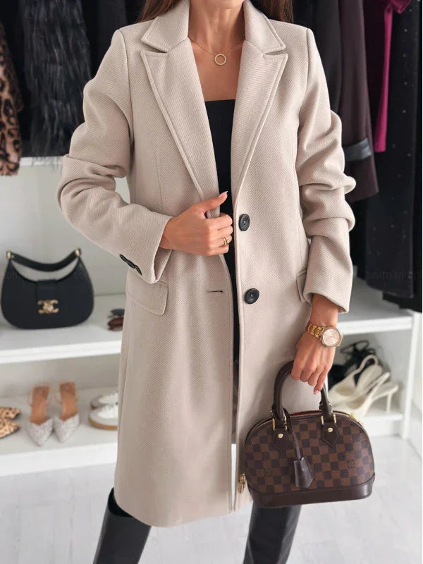Woman in beige tailored coat holding brown checkered designer handbag in stylish boutique setting