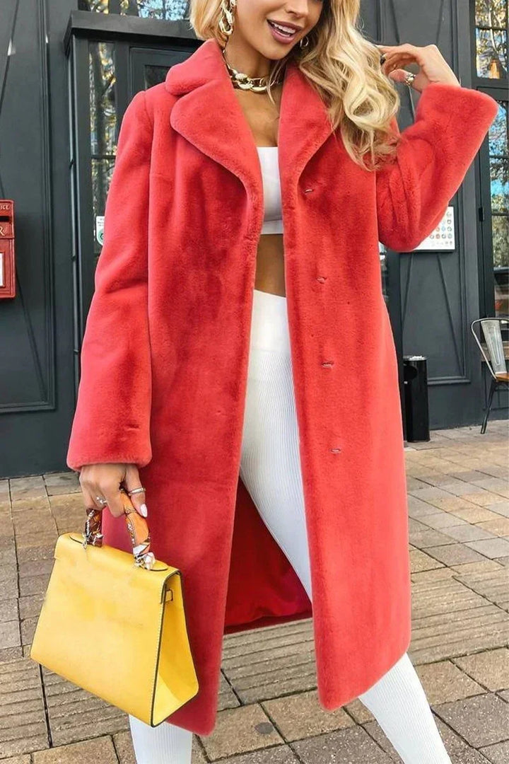 Woman wearing long coral pink faux fur coat, white outfit, holding yellow handbag outside urban building