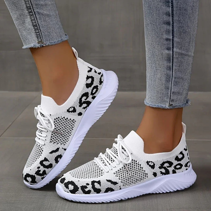 White knitted athletic sneakers with black leopard print worn with light gray jeans on gray floor