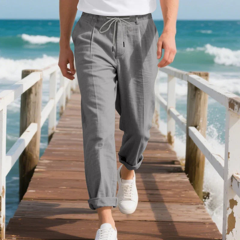 Man wearing casual gray drawstring pants and white sneakers walking on wooden pier by ocean
