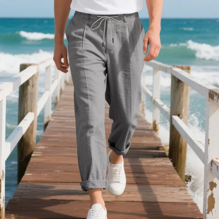 Man wearing casual gray drawstring pants and white sneakers walking on wooden pier by ocean