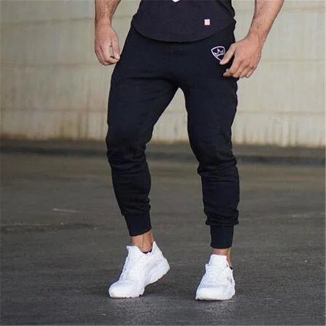 Man wearing black jogger pants with logo on pocket and white sneakers on concrete floor