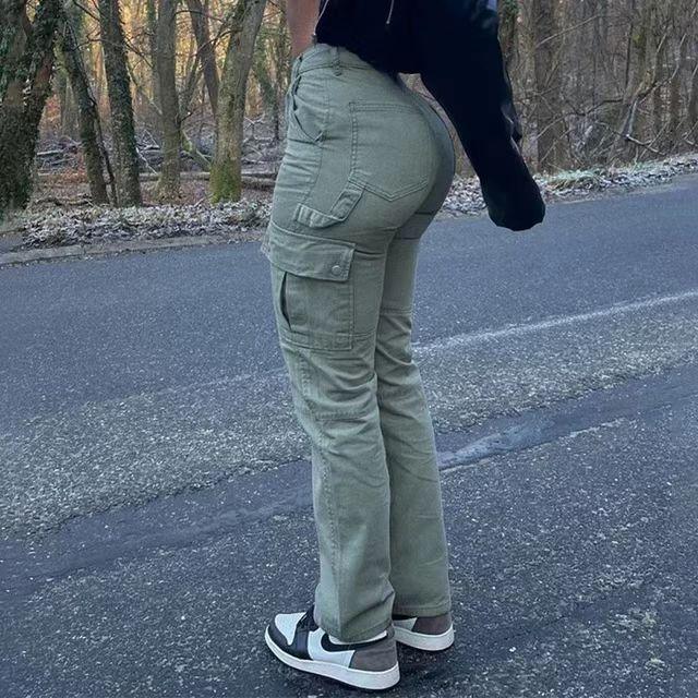 Person wearing green cargo pants and black-and-white sneakers standing on asphalt road with trees in background