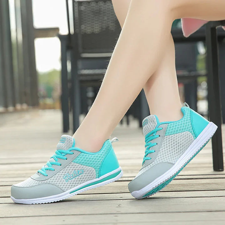 Woman wearing stylish gray and teal athletic sneakers with mesh design on wooden floor