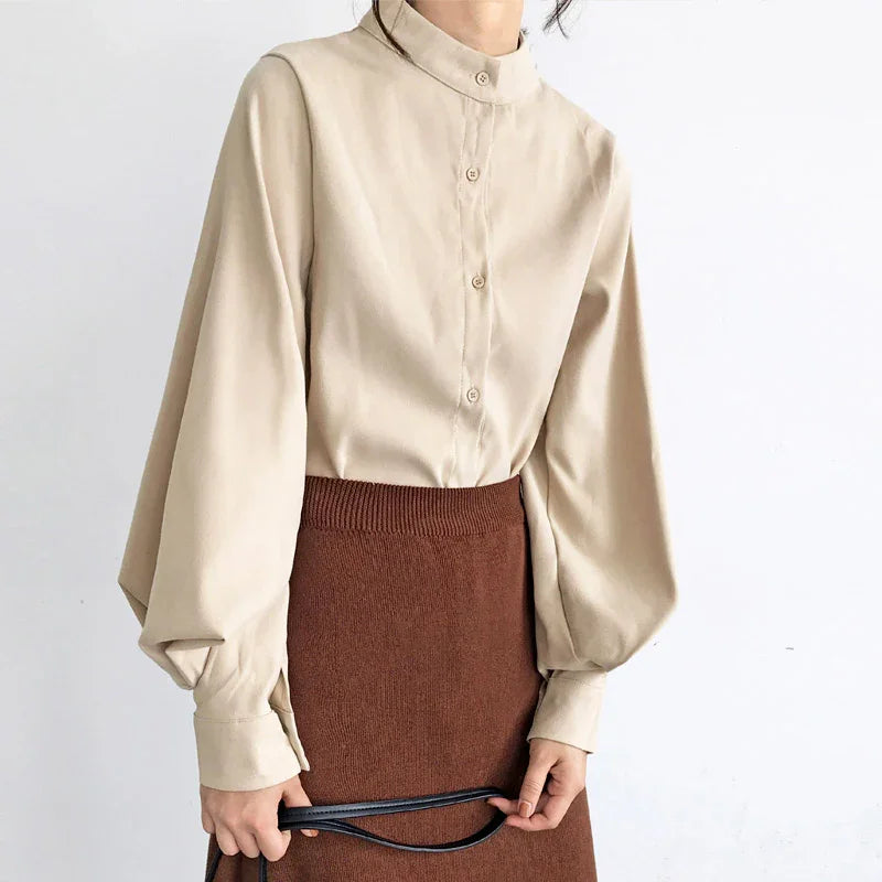 Woman wearing beige button-up blouse with puffed sleeves and brown knit skirt holding black bag strap