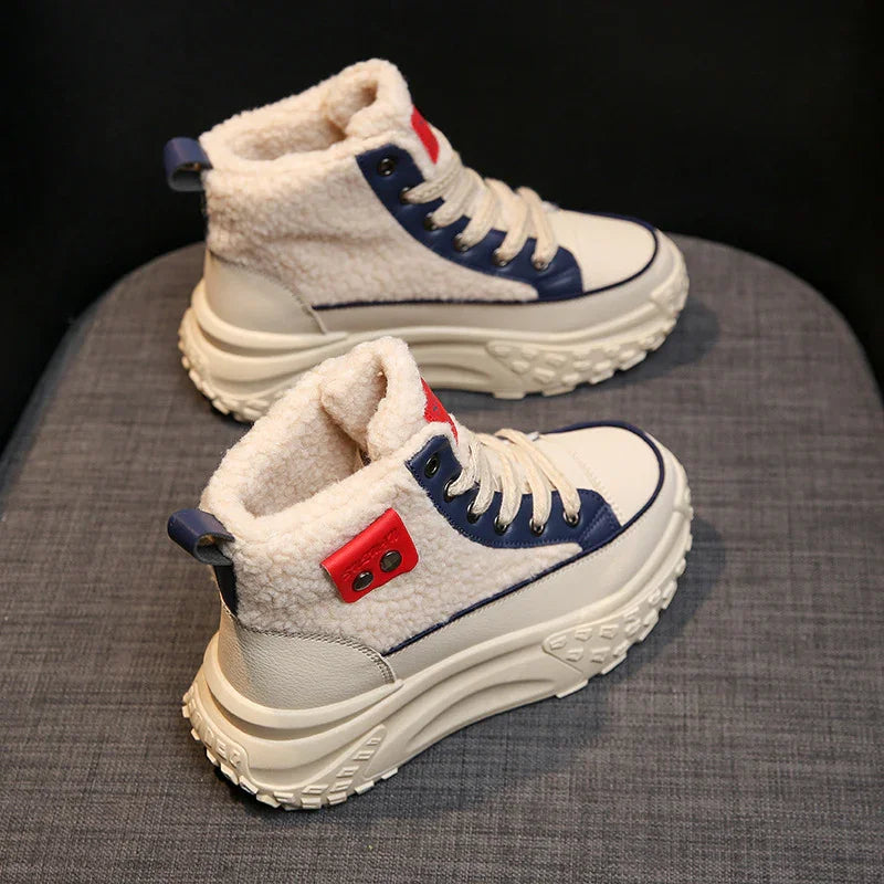 Pair of cream sherpa fleece winter sneakers with chunky soles, blue and red accents on gray fabric
