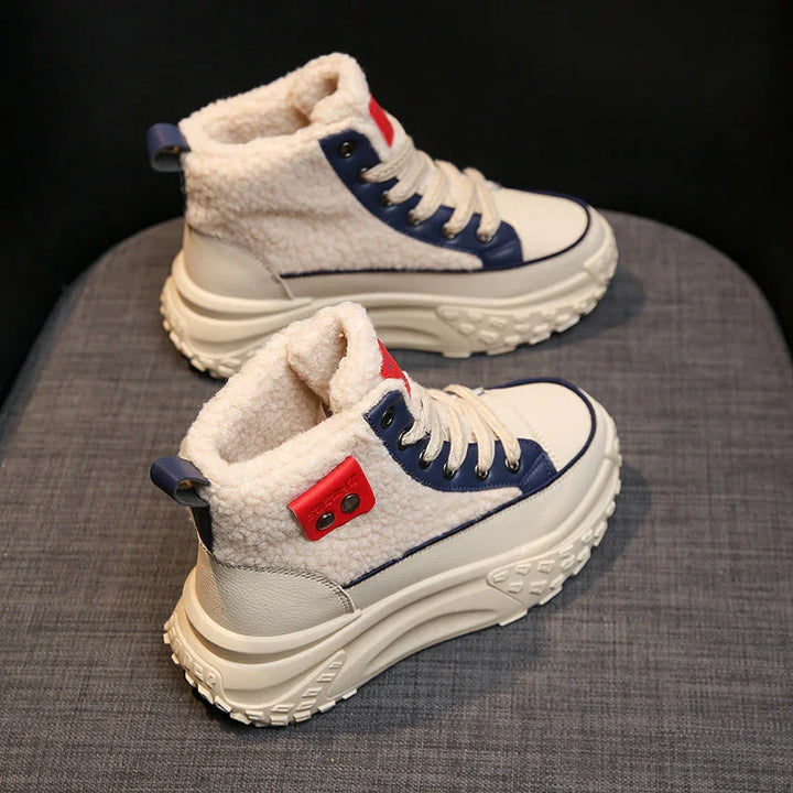 Pair of cream sherpa fleece winter sneakers with chunky soles, blue and red accents on gray fabric