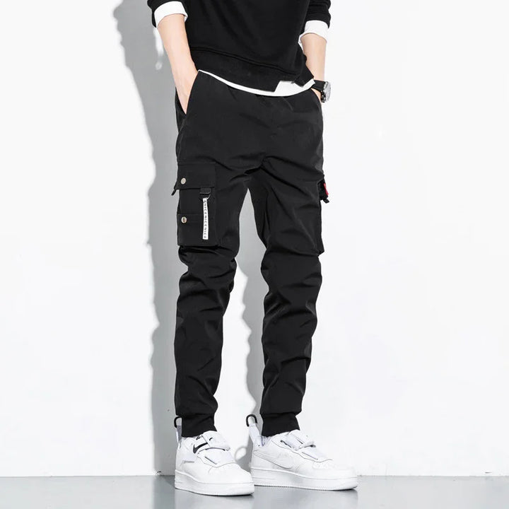 Man wearing black cargo pants with pockets and white sneakers against white background
