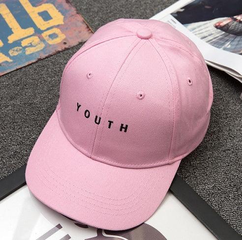 Pink baseball cap with black embroidered word YOUTH on front, placed on textured gray surface