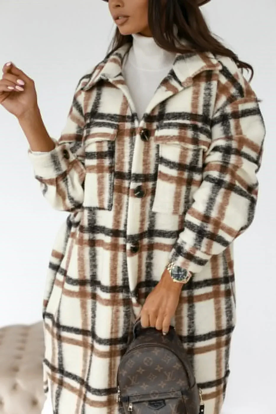 Woman wearing a white brown and black plaid wool coat holding a brown designer backpack