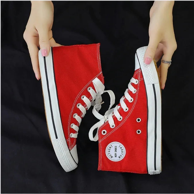 Hands holding red high-top canvas sneakers with white laces and black-striped soles on black background