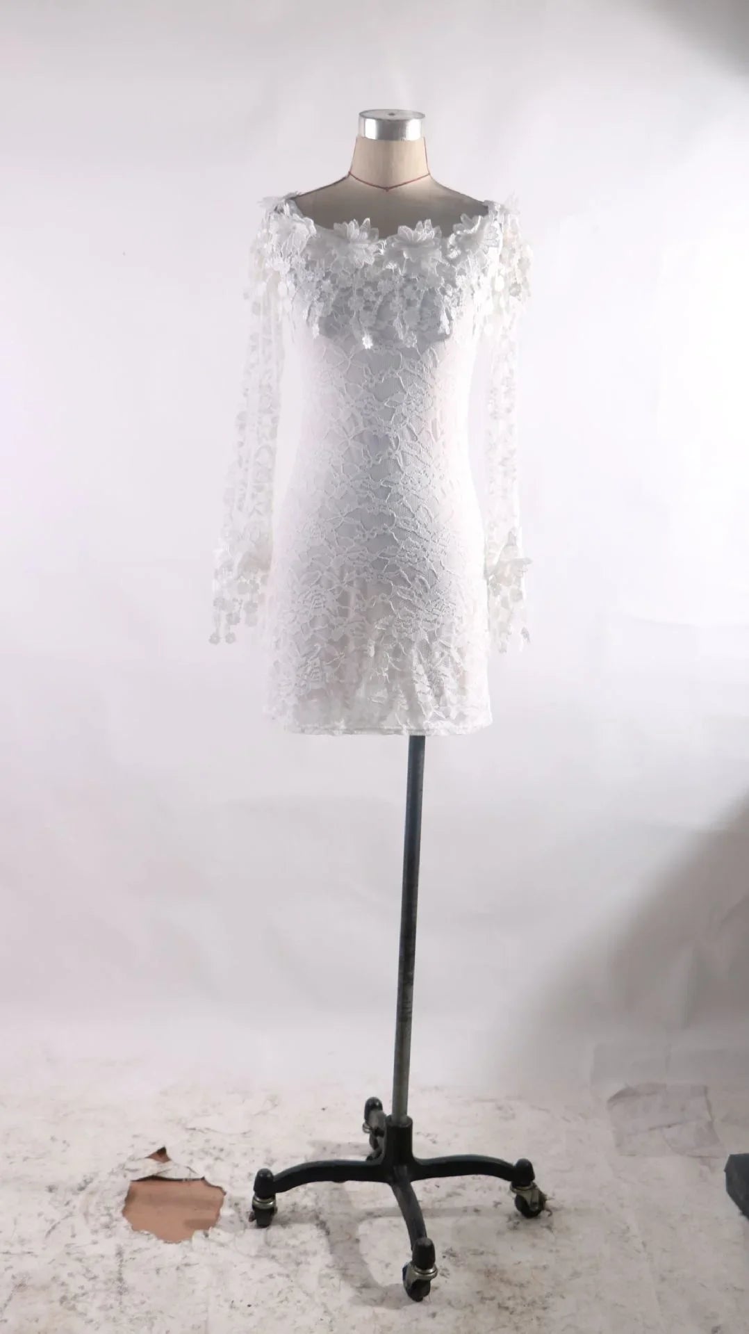 White lace mini dress with floral applique on shoulders displayed on mannequin with wheeled stand
