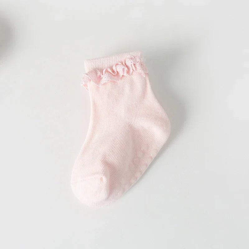 Single light pink baby sock with ruffle trim and non-slip dots on white background