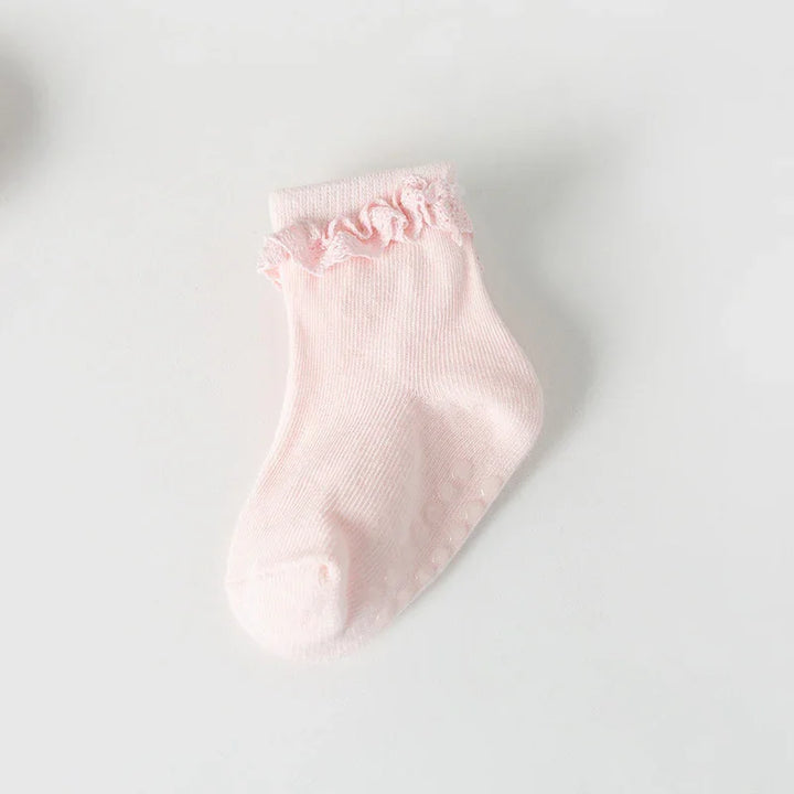 Single light pink baby sock with ruffle trim and non-slip dots on white background