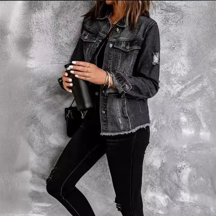 Woman wearing black distressed denim jacket and black jeans holding a black tumbler against gray textured wall