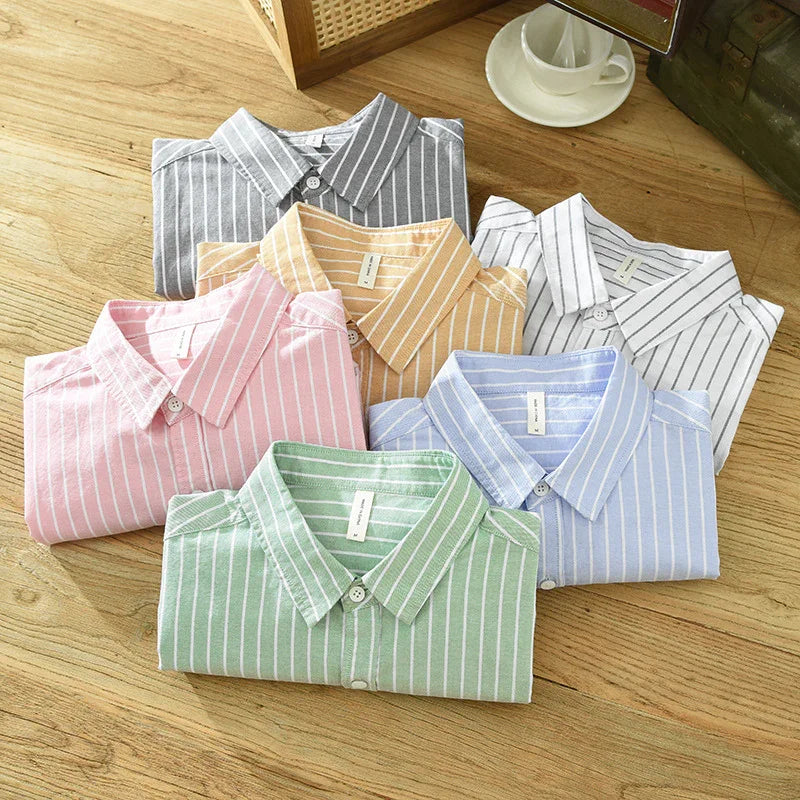 Folded striped button-up shirts in gray, yellow, white, pink, blue, and green on wooden surface