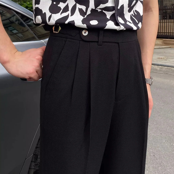 Close-up of black pleated trousers paired with a black and white floral shirt and silver watch