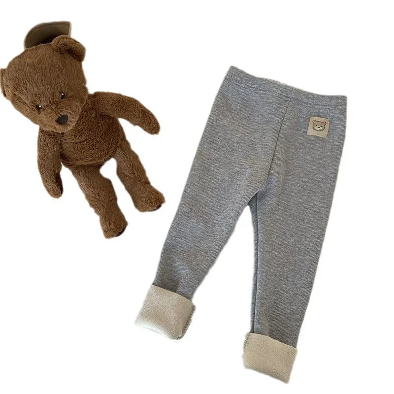 Brown teddy bear plush toy next to gray baby leggings with bear patch and fleece cuffs