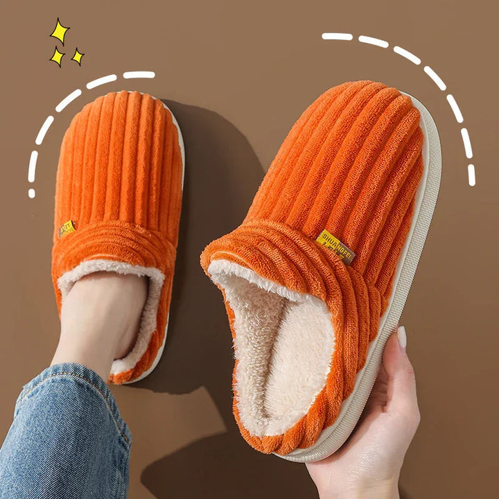 Pair of cozy orange ribbed indoor slippers with soft white fleece lining, worn on foot and held in hand