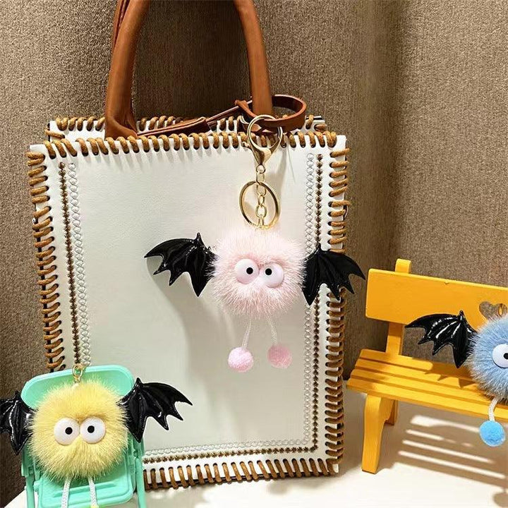 White handbag with brown handles featuring a pink fluffy bat keychain with black wings