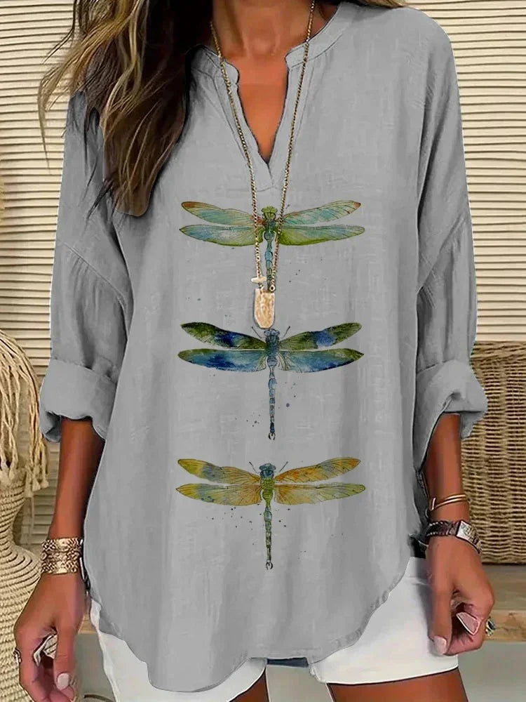 Woman wearing light gray long sleeve top with colorful dragonfly prints, white shorts, and layered necklace
